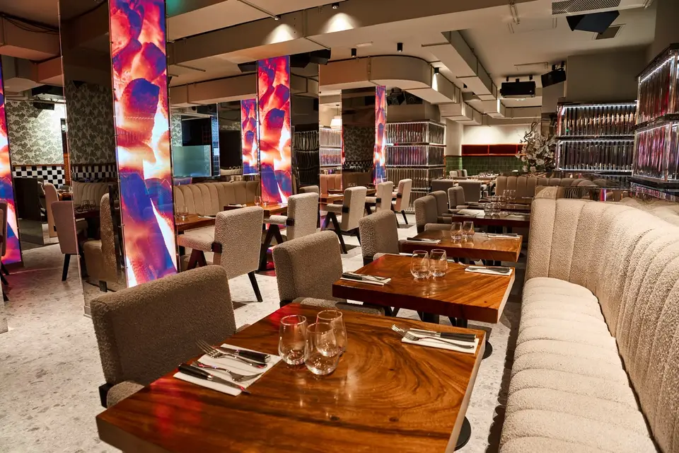 Salle du restaurant avec colonnes lumineuses, tables en bois massif et longue banquette