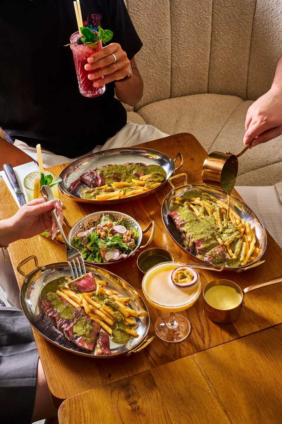 Poêlons de bœuf tranché et de frites nappés de sauce, avec un bol de salade, sur une table en bois du restaurant