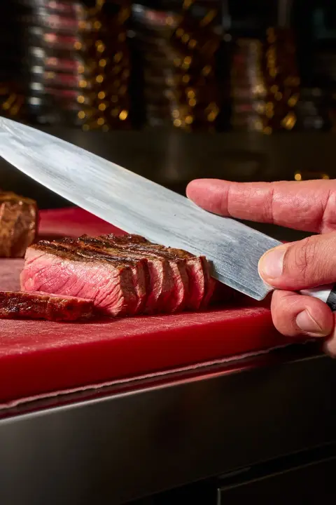 Grilled beef, pink in the middle, sliced with a knife on a red board